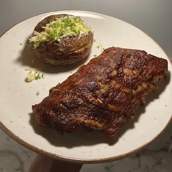 Spare ribs plated with chives, cheese, and sour creme–filled baked potato