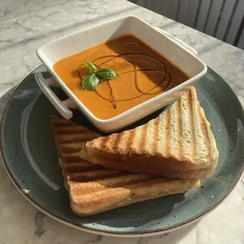 Homemade roast tomato soup drizzled with olive oil and topped with basil, with halved grilled cheese on the side